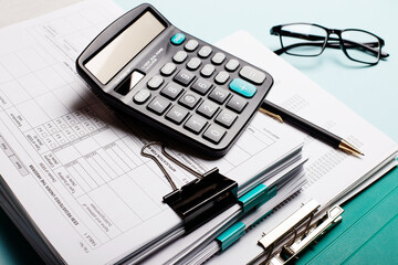 On a blue table are documents stacked, a caculator and paper clips