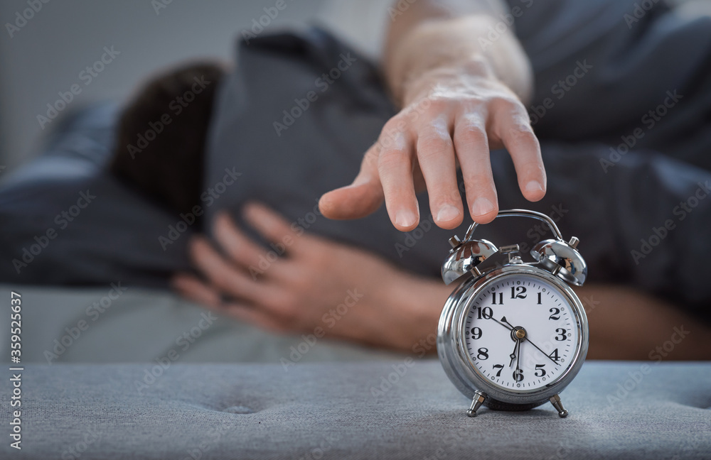 Poster man turning off alarm-clock lying in bed at home