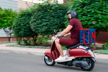 Fototapeta na wymiar Delivery boy wearing red uniform on scooter with isothermal food case box driving fast. Express food delivery service from cafes and restaurants. Courier on the moto scooter delivering food.