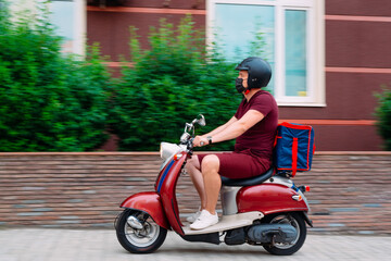 Delivery boy wearing red uniform on scooter with isothermal food case box driving fast. Express food delivery service from cafes and restaurants. Courier on the moto scooter delivering food.