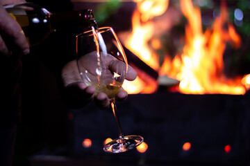 pour a glass of white wine from a bottle on the background of a barbecue with fire