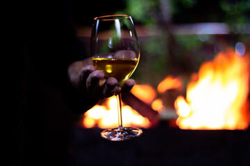pour a glass of white wine from a bottle on the background of a barbecue with fire
