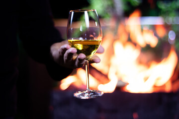 pour a glass of white wine from a bottle on the background of a barbecue with fire