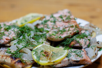 pieces of red fish with lemon on a plate decorated with greens. cooking on the grill.