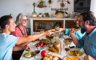 Happy smiling family shares food and drinks at home, having fun together. Table with vegetarian food. Grandmother with son, daughter-in-law and grandson