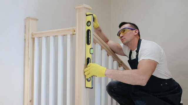Construction male inspector check the vertical level of stairs parts by spirit level, house interior stairs review. Carpenter installs stairs at new modern house