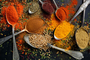 Various spices and herbs on spoons on a black background, top view