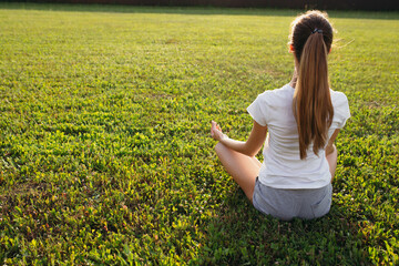 Back to yogi in a t-shirt and shorts with long hair sitting in the Lotus position on the lawn in nature