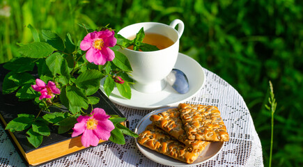 A Cup of green tea with a mint leaf, flowers, and a book on a table in the garden. Evening tea with...