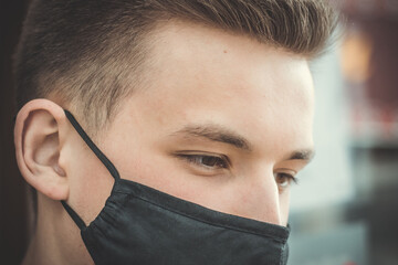 Young guy in a black protective mask. Large portrait of a young man in a medical mask. Pandemic. Coronavirus. Covid 19. Summer 2020. Close-up of the eyes of a young man in a mask.