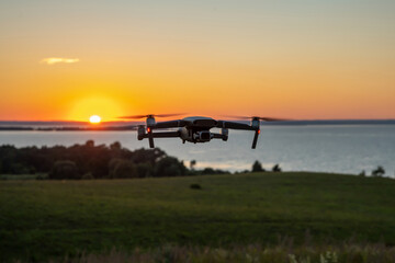 Quadrocopter in flight against the background of the river at the setting sun. The drone's tail lights are on. Copy space.