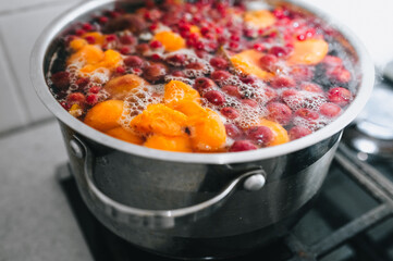 Fresh fruits are boiled in boiling water in a metal pan on the stove. Delicious stewed apricot, apples, cherries, raspberries. Photography, concept.