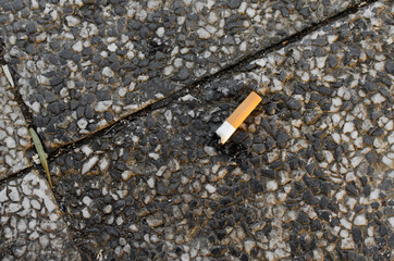 burning cigarette butt, single, isolated on concrete. Cigarette on pavement, close up, top view 