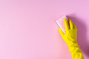 Hand in a yellow rubber glove with a cleaning sponge on a pink background