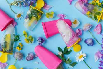 Floral Ice Pops. Hello summer concept. Frozen popsicles and ice cubes made of colorful wildflowers on blue background flat lay with fresh summer flowers