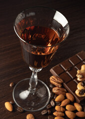 Cognac wine glass with amber cognac, nuts lying near the wine glass, coffe grains, chocolate bar on a dark background.