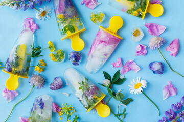Floral Ice Pops. Colorful wildflowers in frozen popsicles and ice cubes on blue background flat lay with fresh summer flowers. Hello summer concept. Creative bright image