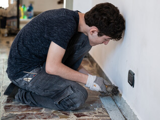 Masonry work in the apartment: a Caucasian boy is wearing work gloves and is using hammer and...