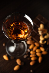 Cognac wine glass with amber cognac, nuts lying near the wine glass, coffe grains, chocolate bar on a dark background. View from the top.