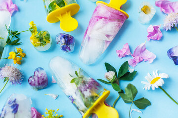 Floral Ice Pops. Frozen popsicles and ice cubes made of colorful wildflowers on blue background flat lay with fresh summer flowers. Hello summer concept. Refreshing vegan sweets