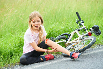 Sad crying little child girl fell from the bike in the summer park. Bleeding on hands and feet. Bicycle accident. Injuries while cycling. Accidents and injuries to children during summer activities