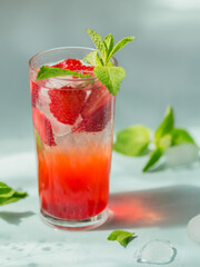 Glass of strawberry cocktail or mocktail, refreshing summer drink with crushed ice and sparkling water on light background.