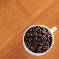 White Cup with dark brown coffee beans on the background of the table.