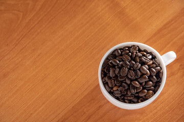 White Cup with dark brown coffee beans on the background of the table.