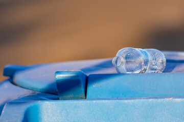 Plastic water bottle left on top of blue recycle can
