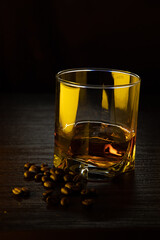 A glass of cognac. A glass of cognac in gold-amber light with grains of coffee near the glass.