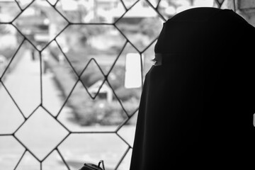 Muslim woman in burka watching outside of the window.
