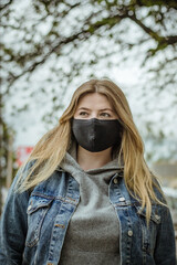 Closeup portrait of a girl in a medical mask. Quarantine of a pandemic coronavirus. Covid 19. A student in a protective mask. Young girl with long hair in a black protective mask in the city. 2020.