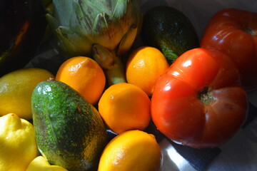 Close-up of colorful fresh fruit and vegetables, including red tomato, yellow lemons, green avocado, and artichoke, water droplets on tomatoes.