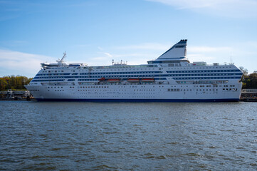 Large white passenger RORO-ferry with blue stripes docked at the harbor.