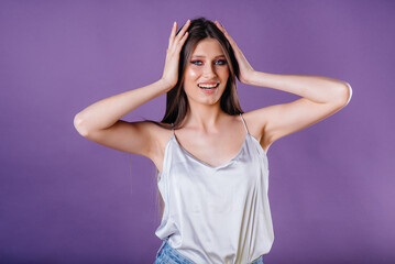 Fototapeta premium A young beautiful girl shows emotions and smiles in the Studio on a purple background. Girls for advertising