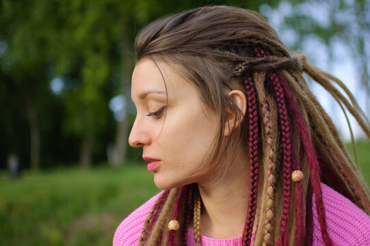 Outdoors female portrait of a modern girl with dreadlocks wearing pink sweater and dark jeans in a city park during a sunset, be free, be youself concept