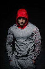 A sporty guy stands in the Studio against a dark background in a hood. Sports, beauty