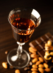Cognac wine glass with amber cognac, nuts lying near the wine glass, coffe grains, chocolate bar on a dark background.