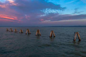 Wooden poles like breakwaters on Lake Neusiedl in Podersdorf, Austria. In the background is a dramatic sky at sunrise.