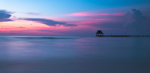 Fototapeta na wymiar Isla Mujeres sunset on the beach with a small wooden cottage at the end of a pier in Mexico.
