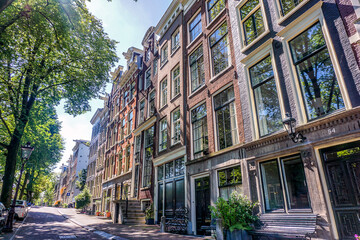 Amsterdam canal houses facades with vibrant trees on sunny summer day