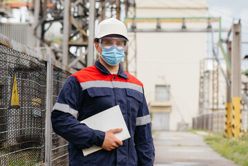 Fototapeta na wymiar An electrical substation engineer inspects modern high-voltage equipment in a mask at the time of pondemia. Energy. Industry