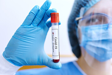 Obraz premium Hand in blue gloves holding a tube with test blood covid-19. Covid-19 diagnostic in clinic. Test tube with blood sample for COVID-19 test. Positive test result. 