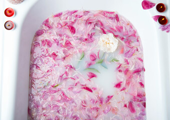 Peony petals in a water with milk bathtub with some candles. Spa background photo. © Eliada