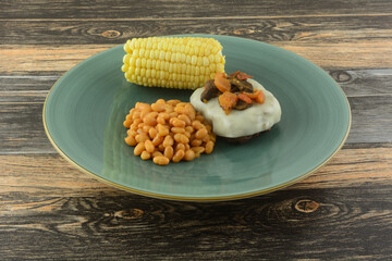 Hamburger covered with melted provolone cheese topped with mushrooms and tomatoes, baled beans, corn on the cob for meal on blue plate