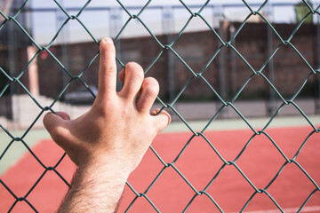 Hand grasping a green wired fence