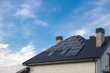 Solar panel on a black roof with two chimney against cloudy blue sky