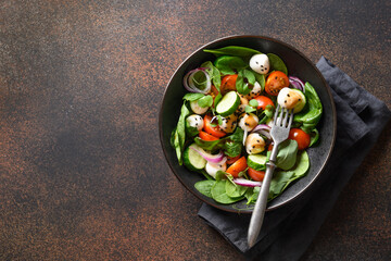 Homemade salad with spinach, cherry tomatoes, basil, onion and Mozzarella. Vegan food. Tasty and healthy meal on brown background. Top view. Copy space.