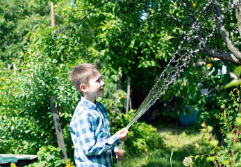 a child in a blue plaid shirt, watering the garden with a garden hose.