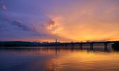 Fototapeta na wymiar Orange blue sunset on the Dnieper river in Kyiv. Panorama of the bridge. Clouds in the sky.